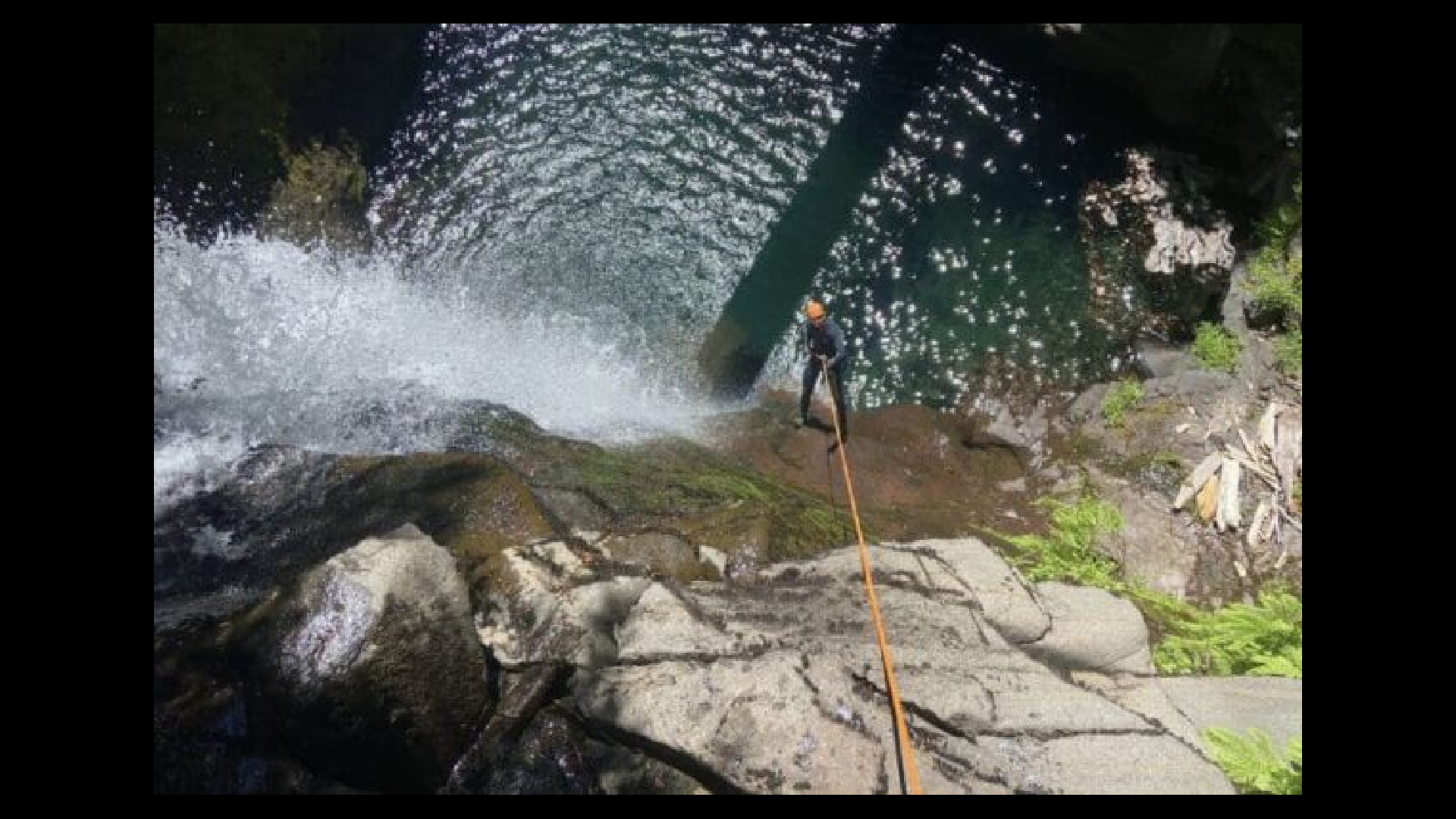 a person rappelling down a cliff into a pool of blue green water