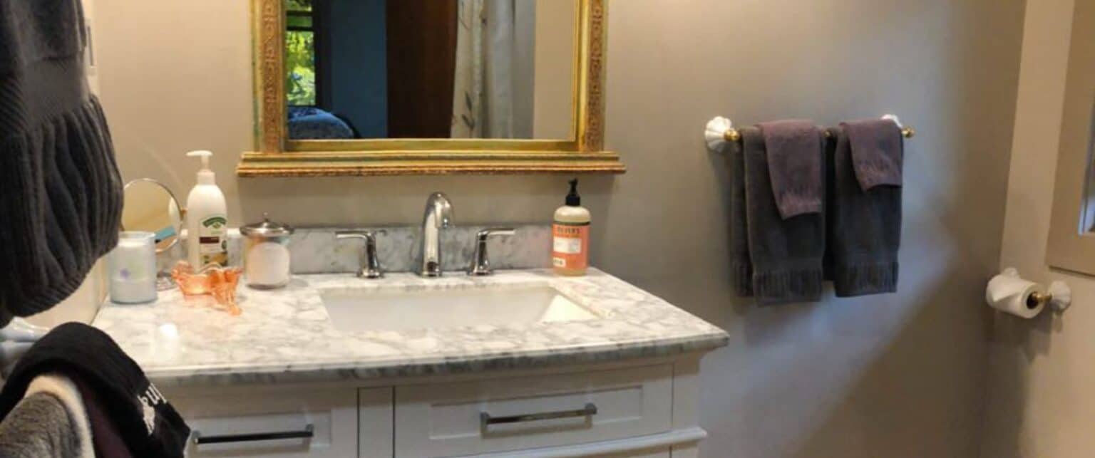 A bathroom sink area with marble countertop, gold-framed mirror, and towels