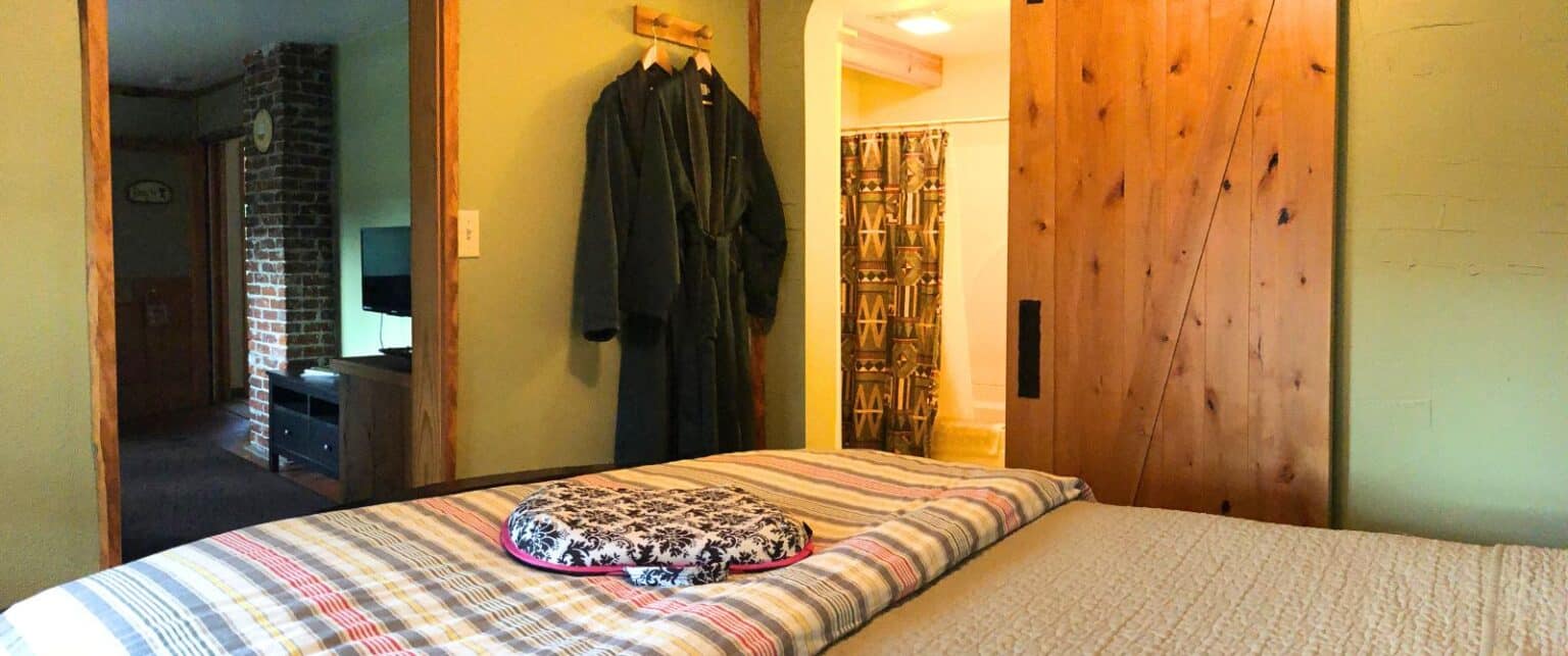 A wide view of a bedroom with a plaid bedspread, a robe hanging on the wall, and a doorway leading to a bathroom and another room.