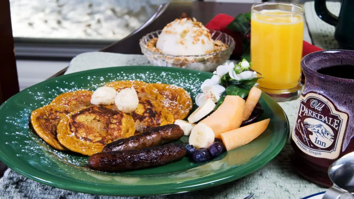 A breakfast plate with pancakes, sausage, fruit, and a cup of coffee.